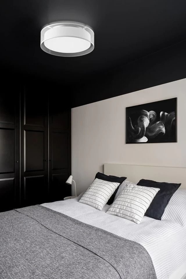 A dark, moody bedroom with a flush-mount light and soft gray bedding