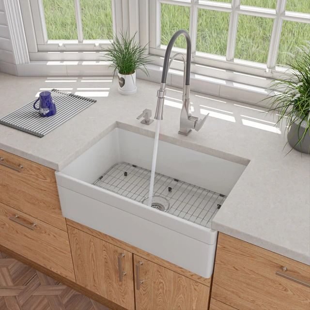 White farmhouse sink with a tall chrome faucet and oak cabinets