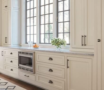 Cream kitchen cabinets with dark metal pulls and tall windows