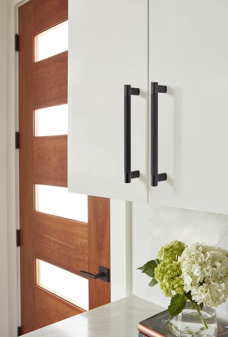 White bathroom cabinets with black pulls and a warm wood door