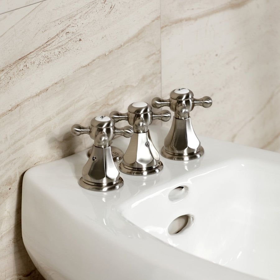 Polished nickel three-handle faucet on a white bidet
