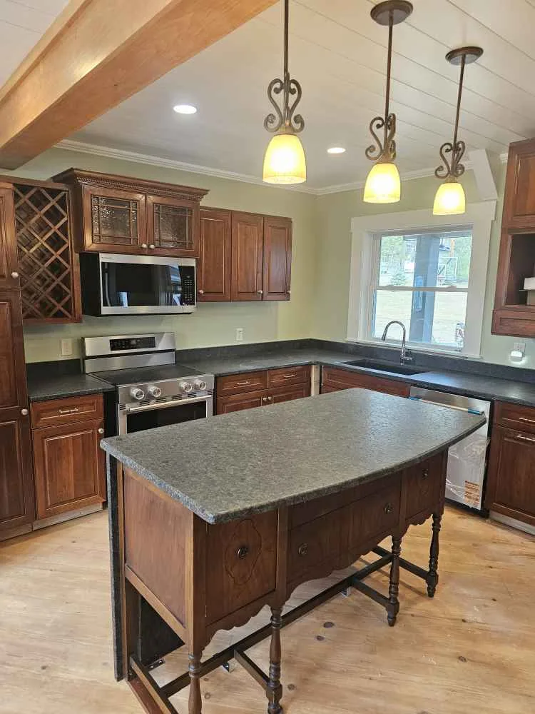 A kitchen with a large granite island, wood cabinets and pendant lights