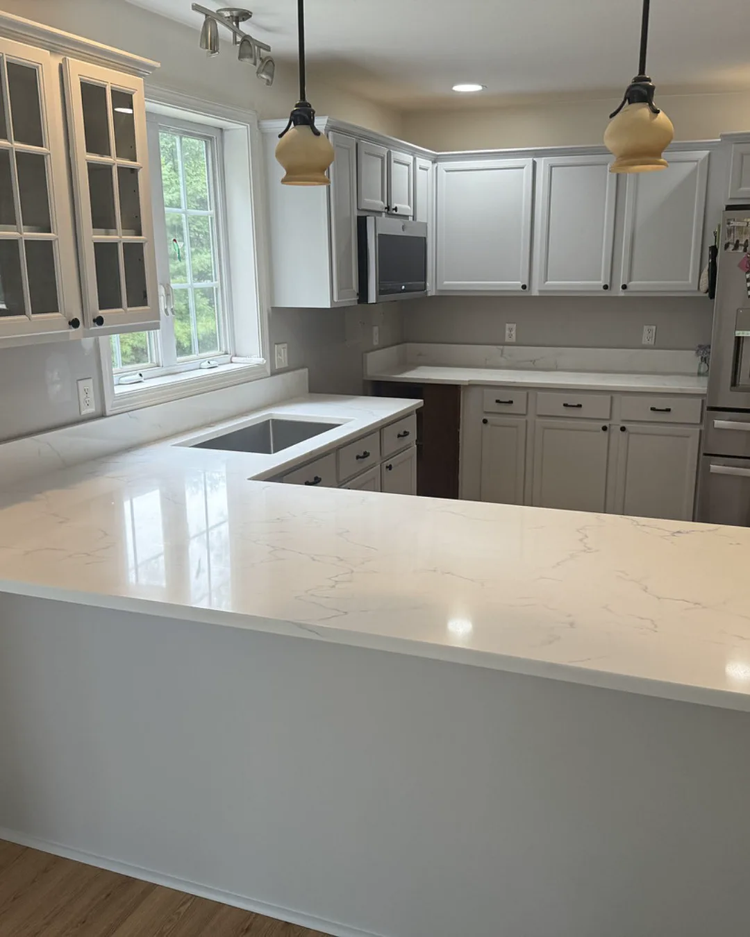 A white apron-front farmhouse sink set into a quartz countertop